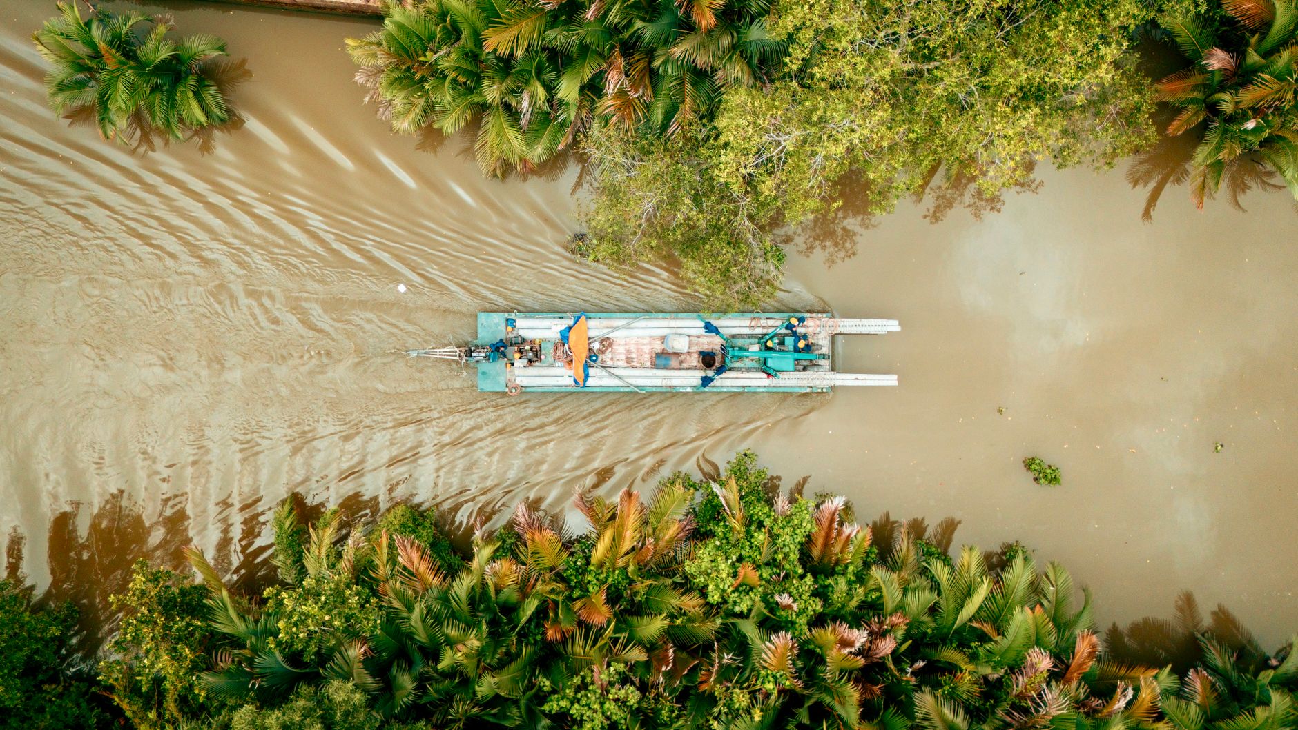 Aerial shot of a boat navigating a river surrounded by lush Vietnamese jungle.