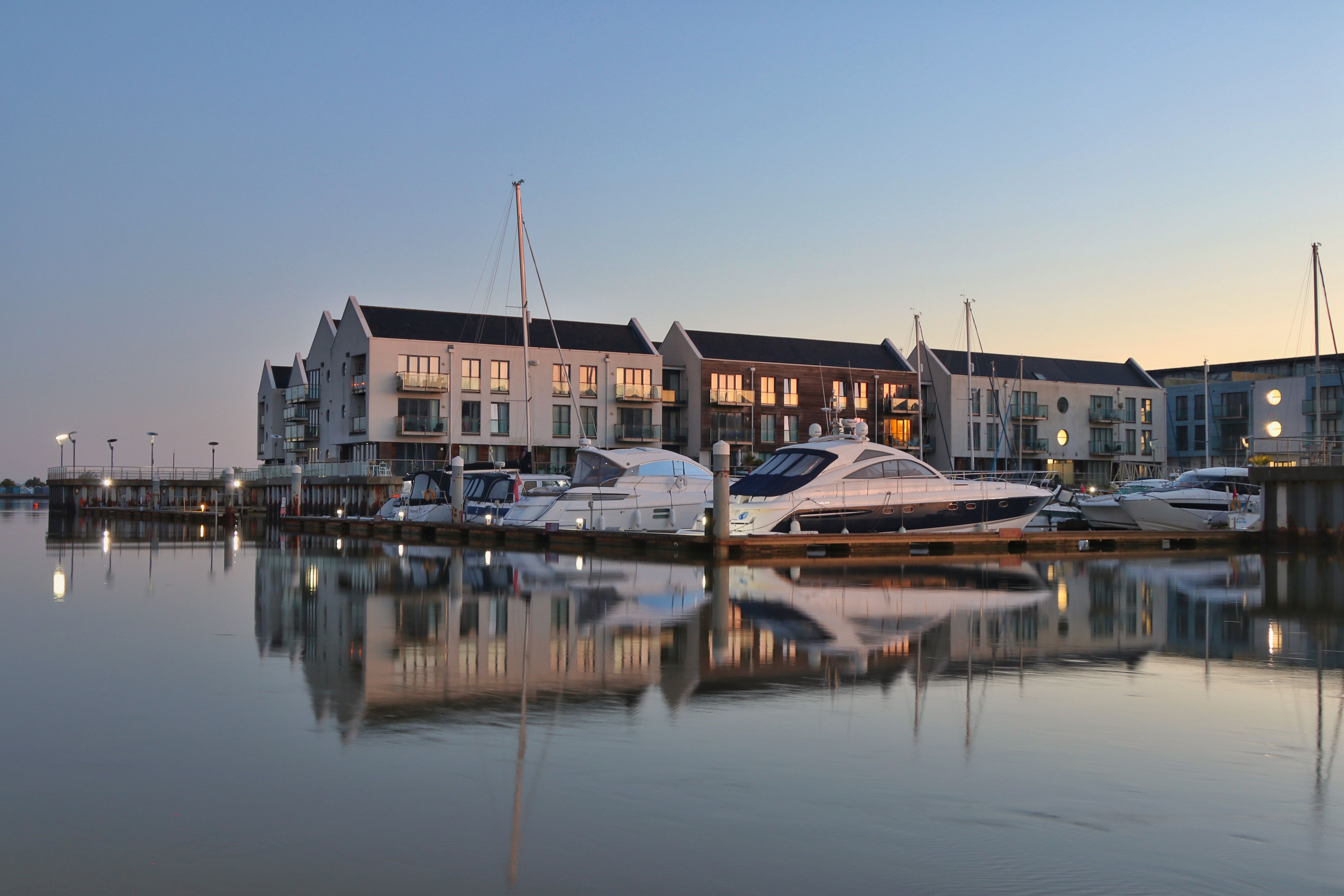 View of boats docked at a marina with reflections and architecture, Brightlingsea, UK, at sunset.