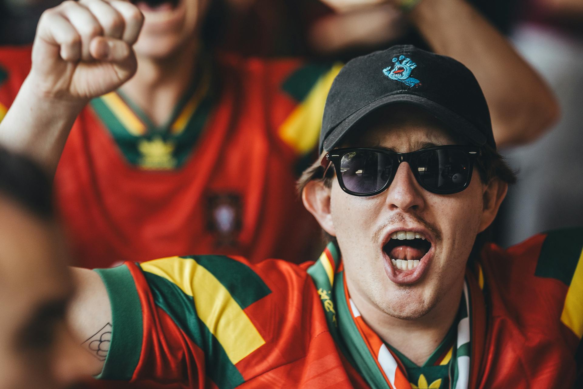 Passionate sports fans cheering in colorful jerseys and sunglasses at a lively match.