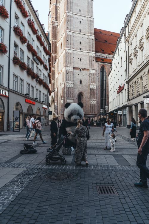 Free People gather around person in panda suit in busy city square near historic church. Stock Photo