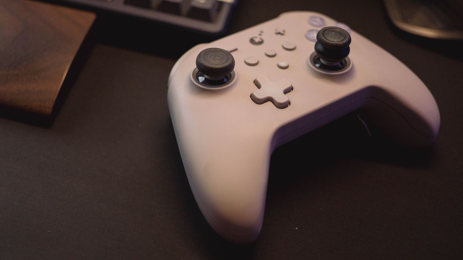 A white game controller on a dark desk beside a keyboard