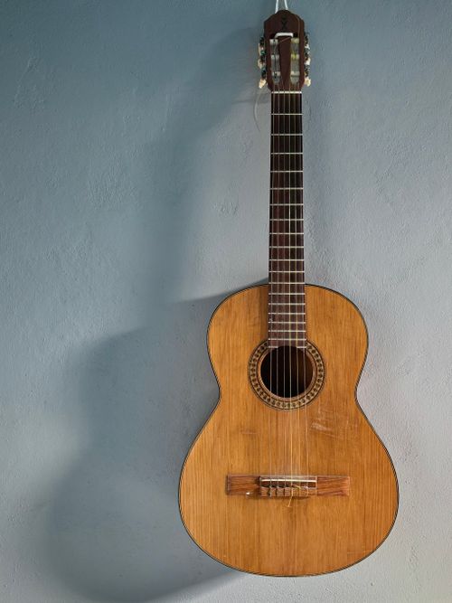 Free A vintage classical guitar with wooden body hanging against a blue wall. Stock Photo