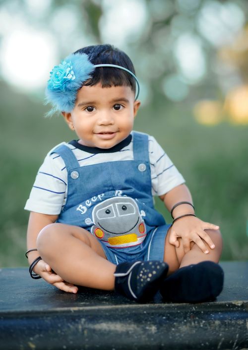 Free Cute baby sitting outdoors wearing blue overalls and a headband, enjoying a sunny day. Stock Photo