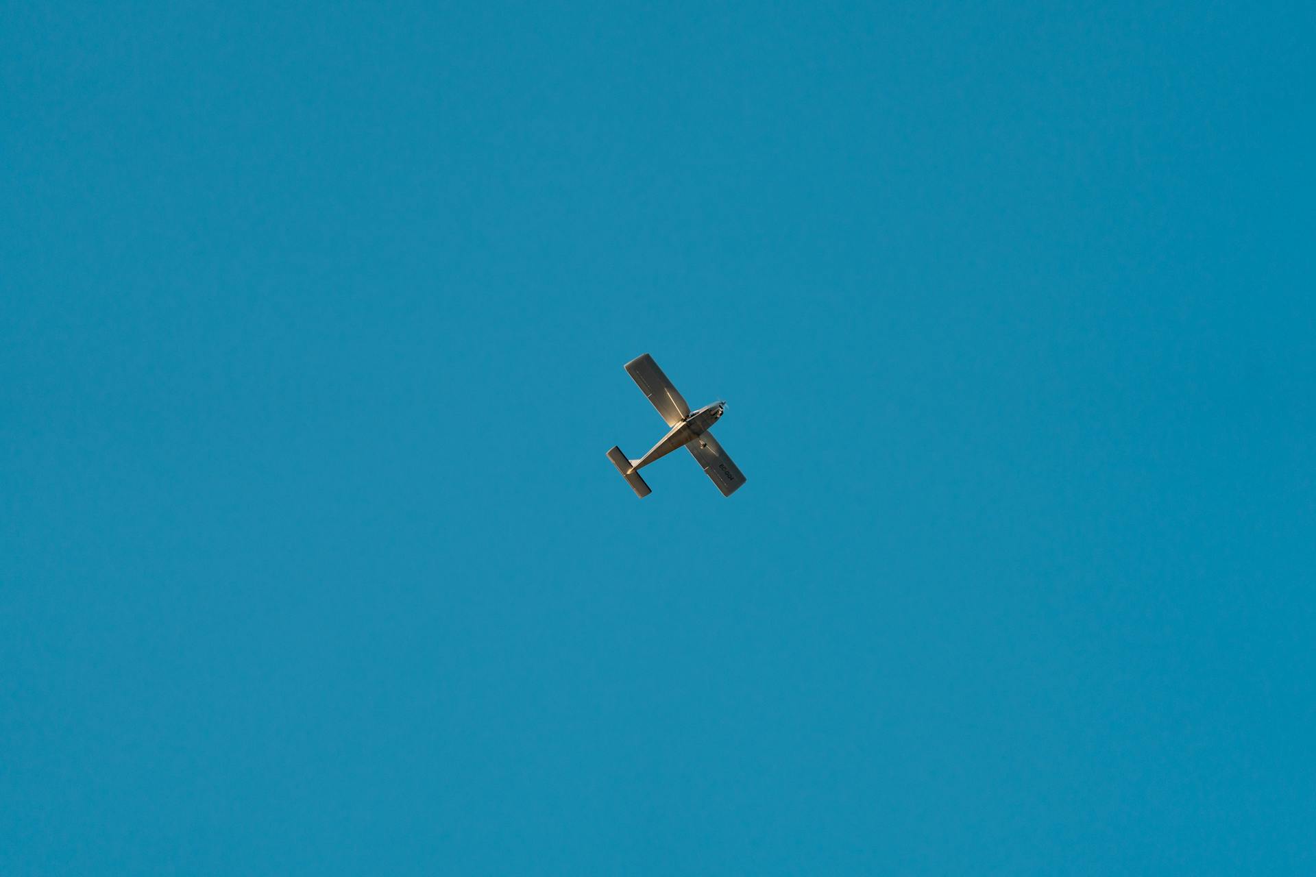 A small aircraft flying high with a clear blue sky as the background, symbolizing freedom and travel.