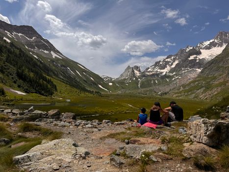 A family enjoys a summer hike through scenic mountains, showcasing snow-capped peaks.