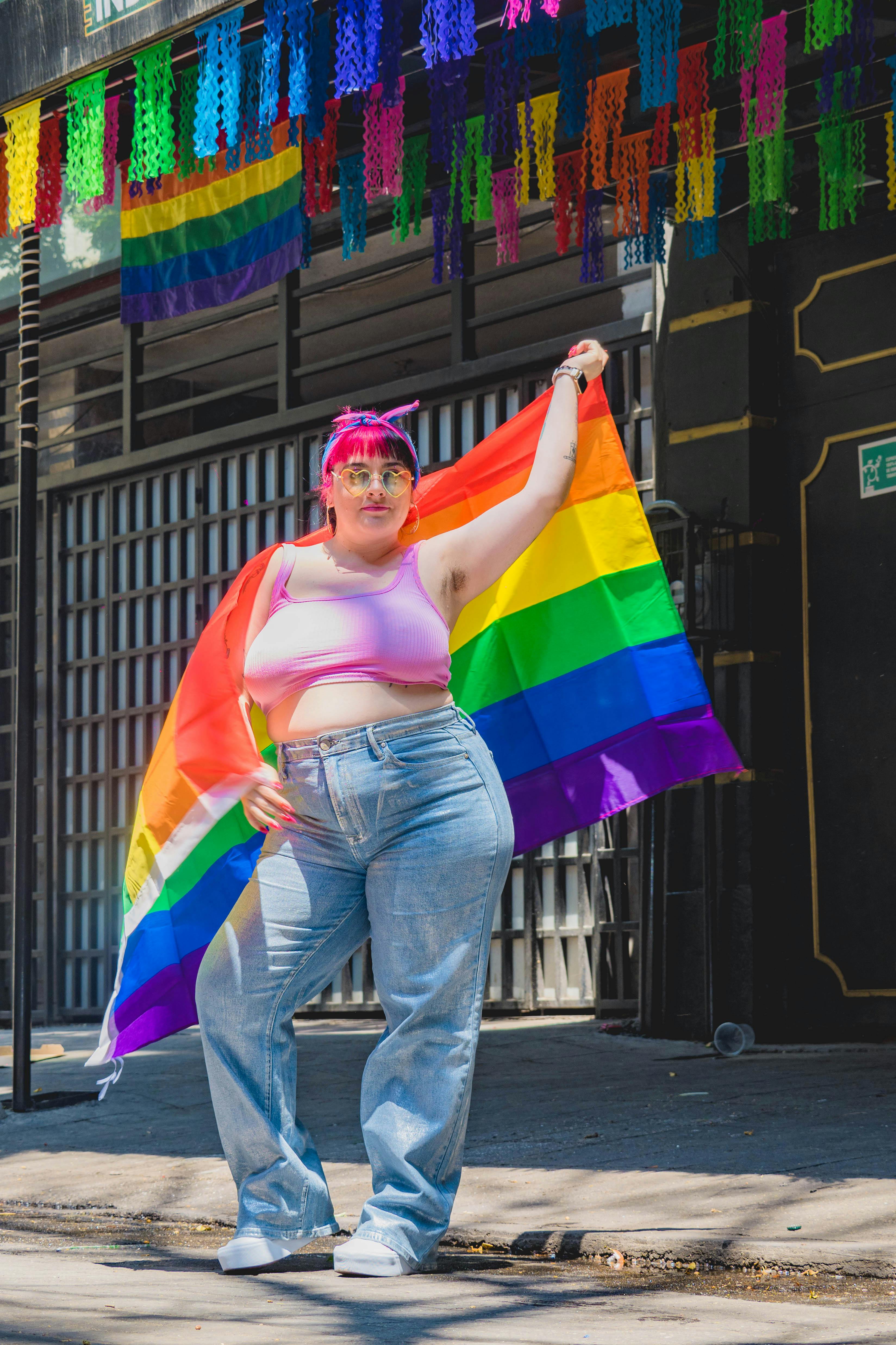 A woman in a pink top and jeans holding a rainbow flag