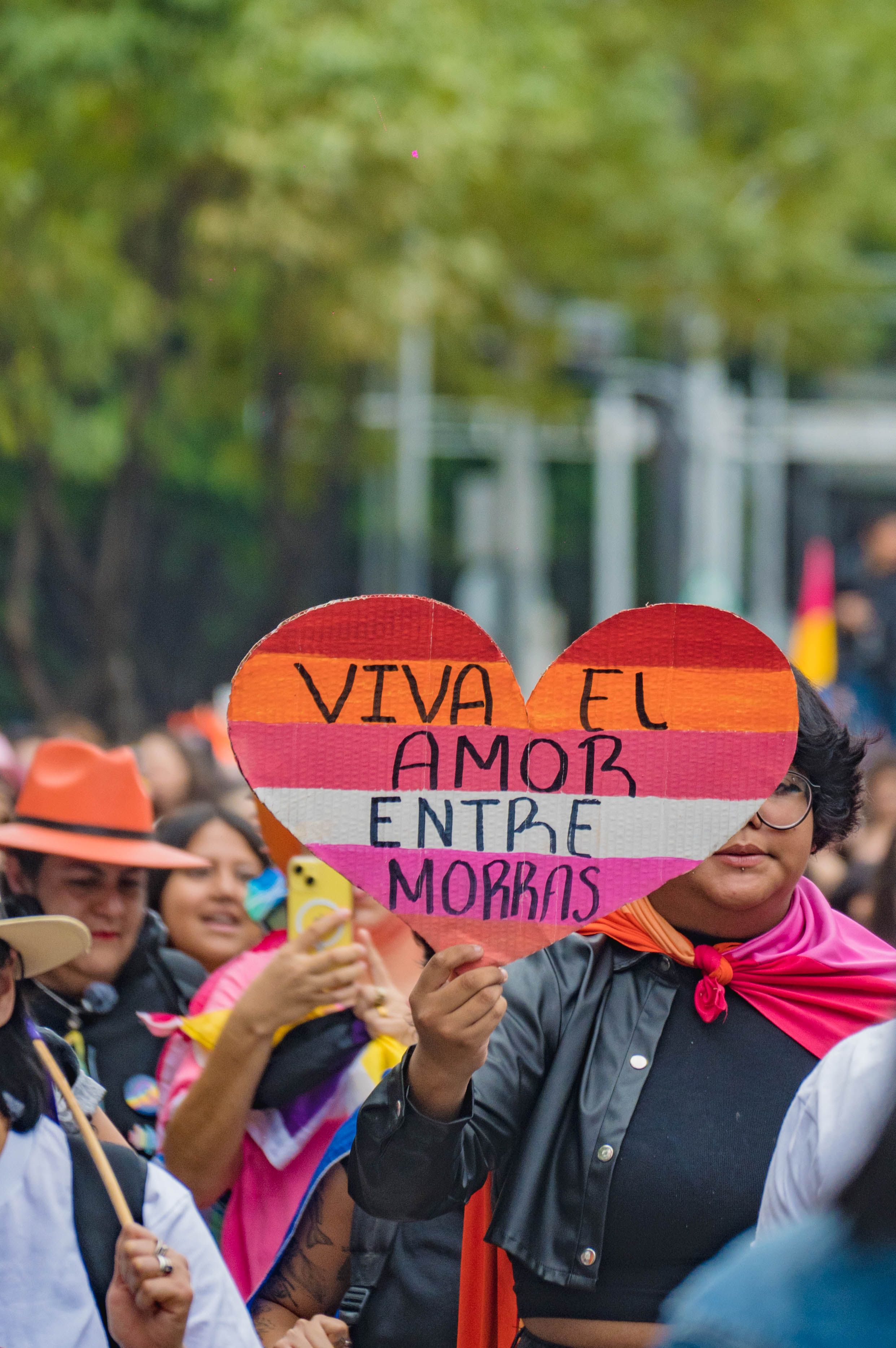 People celebrating at a vibrant pride parade with heart-shaped sign promoting love.