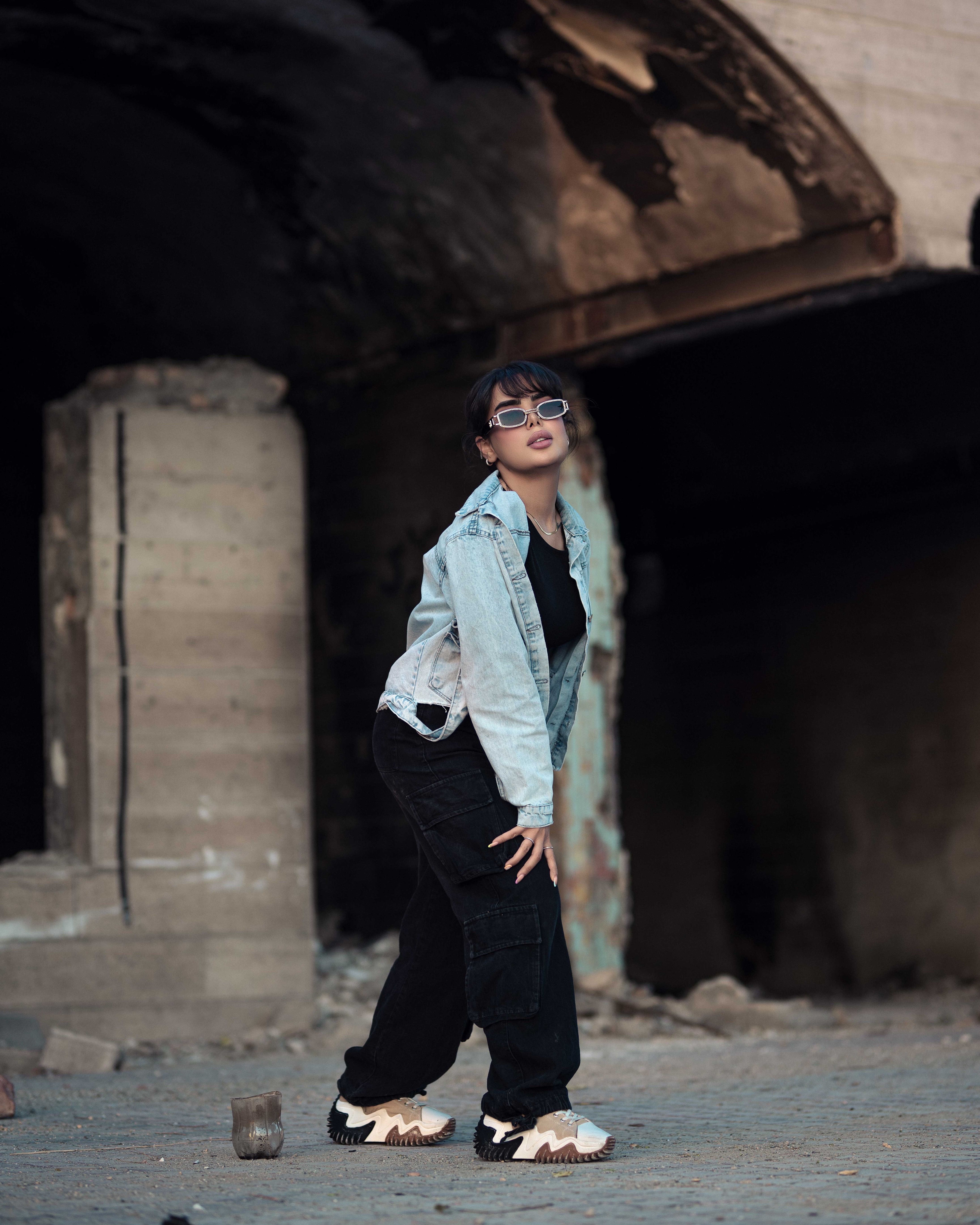 Stylish woman posing in an urban setting wearing denim and sunglasses, exuding street fashion vibes.