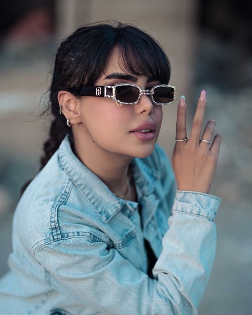 Free Young woman with sunglasses and denim jacket making peace sign outdoors. Stock Photo