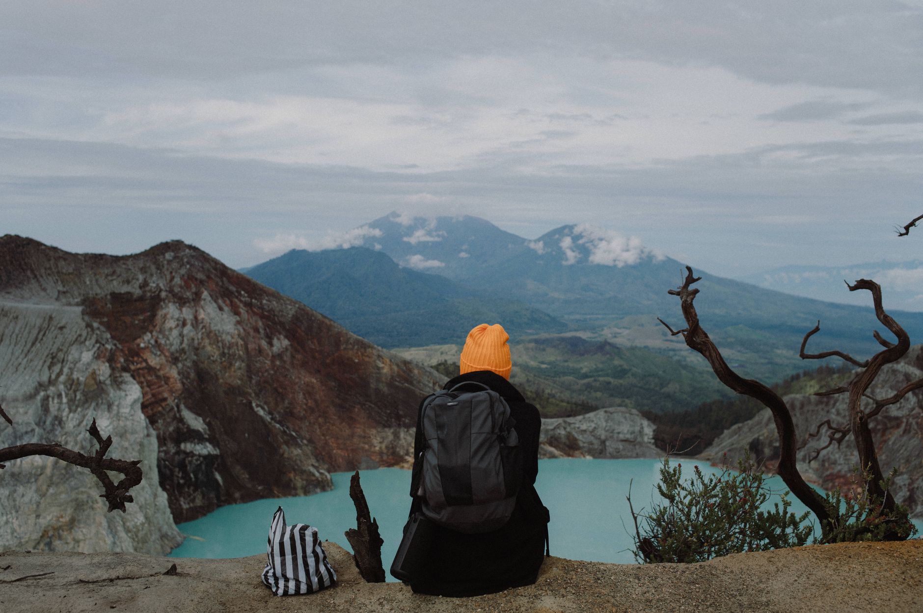 A traveler sits by the stunning Kawah Ijen crater lake in East Java, Indonesia, surrounded by rugged volcanic landscape.