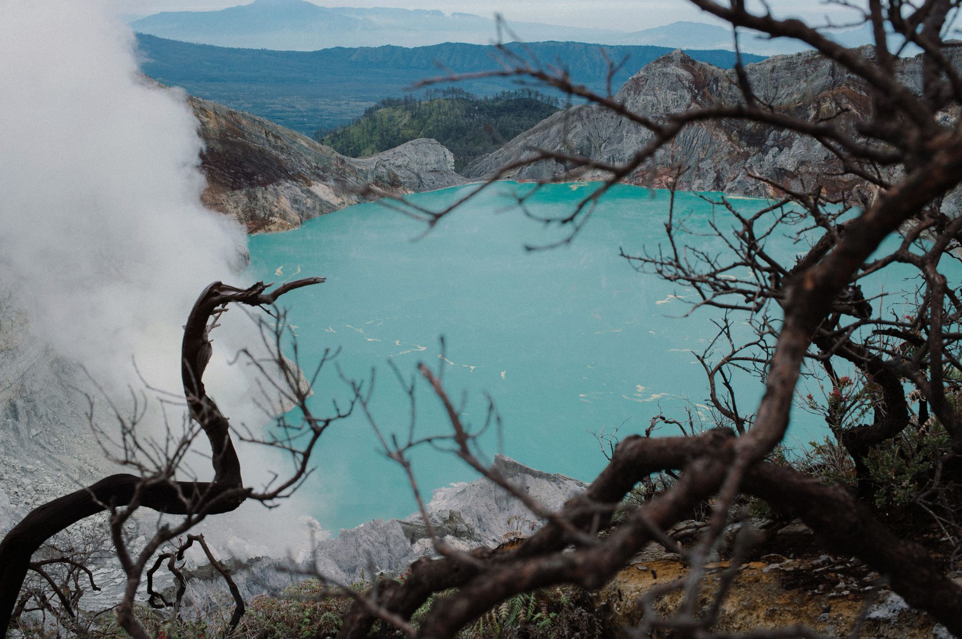 Dramatic view of Ijen Crater's turquoise lake surrounded by rugged terrain and mist.