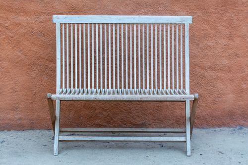 Free An antique wooden bench stands in front of a textured orange wall, showcasing rustic charm. Stock Photo