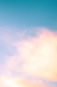 A beautiful sunset sky with soft clouds and an airplane contrail stretching across vibrant hues.