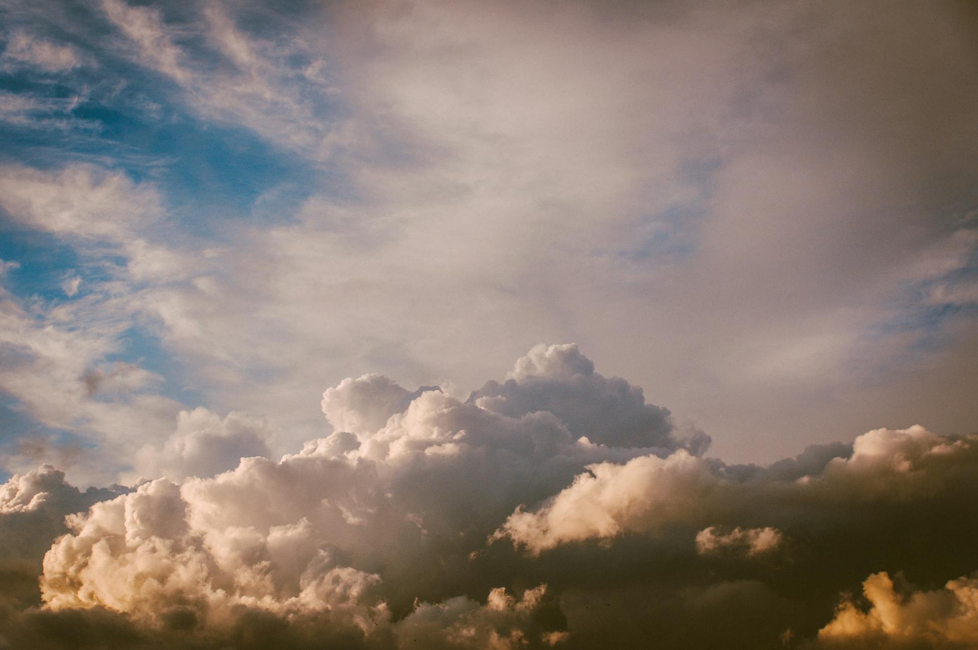 A moody sky showcasing cumulus clouds during sunset with a warm glow.