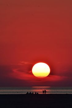 Dramatic sunset over the ocean with silhouetted figures on the beach.