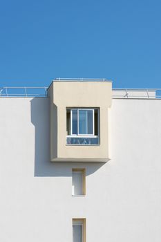 Simple view of a modern building facade with a window against a clear blue sky.