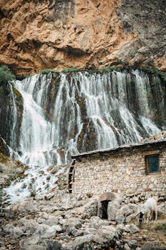 Breathtaking view of a cascading waterfall next to a rustic stone house in Kapuzbaşı, Türkiye.