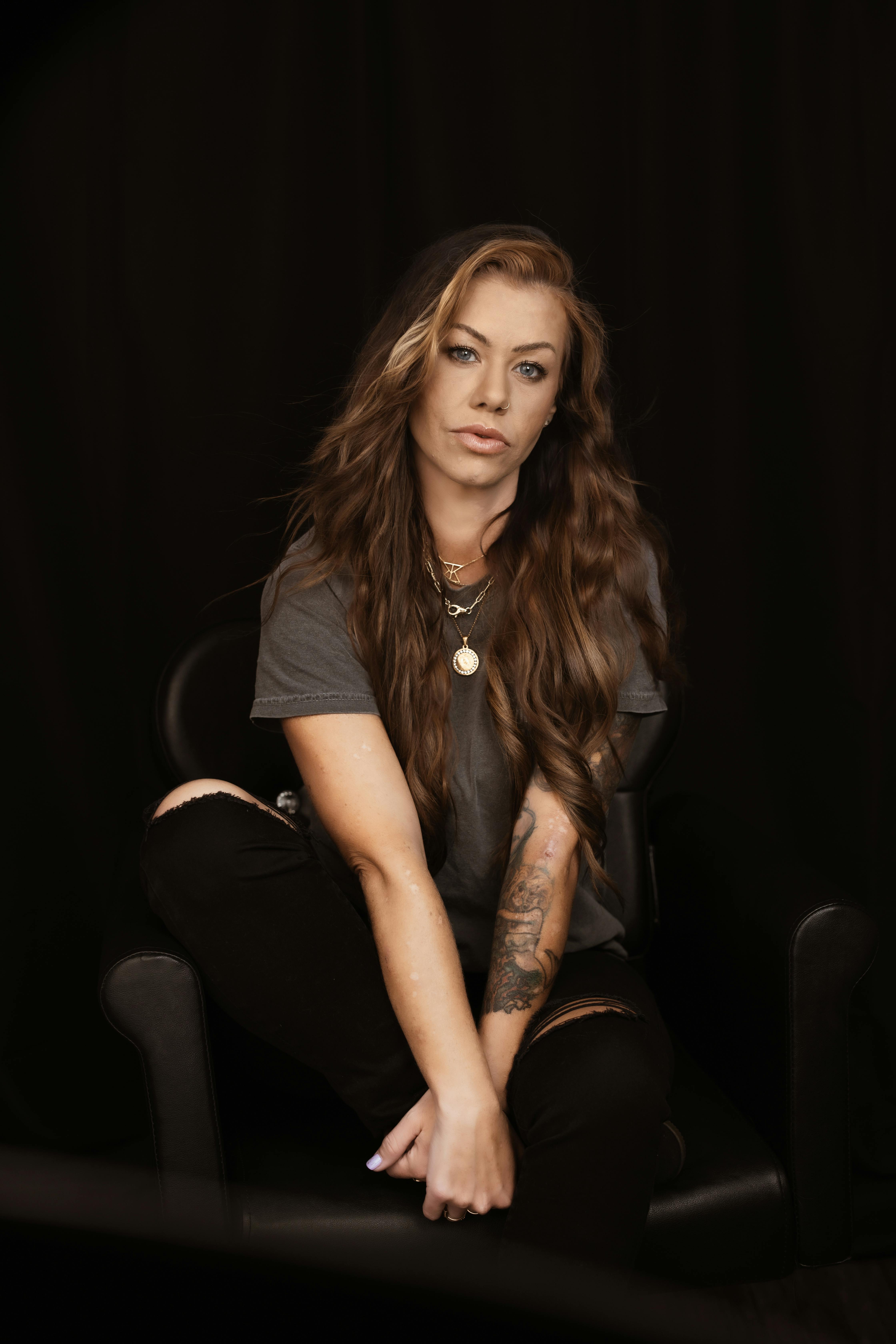 Studio portrait of a woman with long hair and tattoos against a dark background.