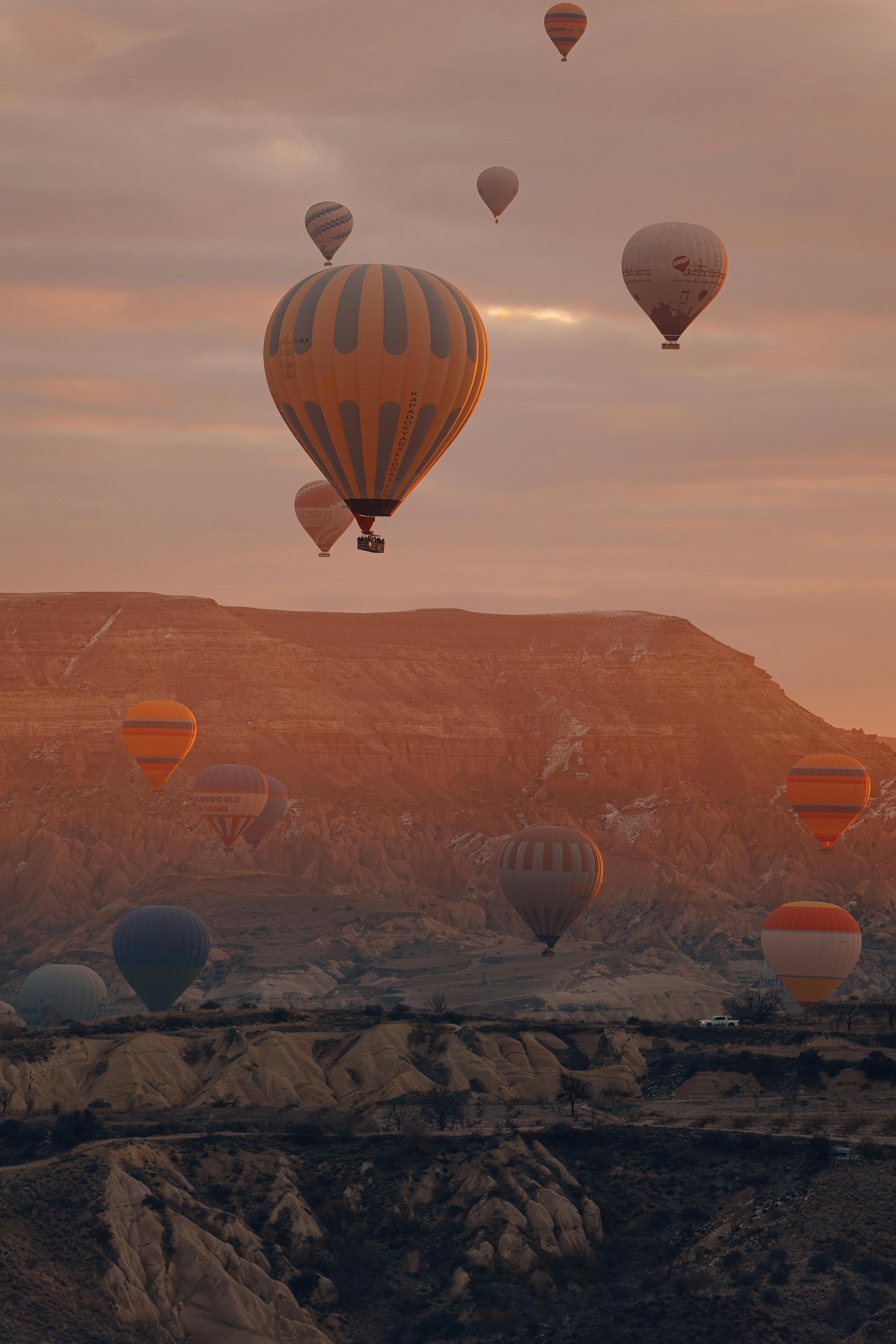 Hot air balloons float over the rocky landscape of Cappadocia, Türkiye, during sunset, creating a serene view.