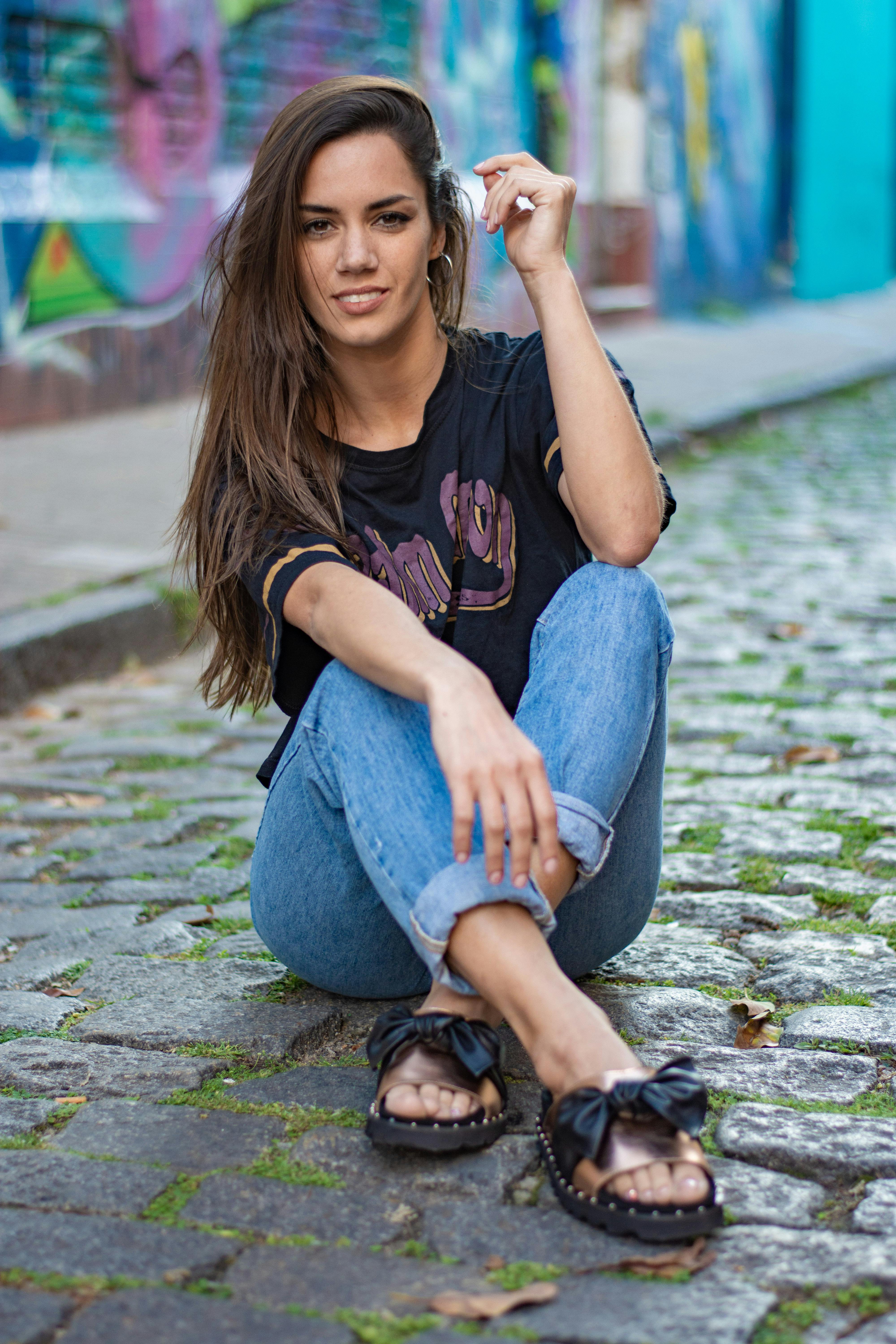 a woman sitting on the ground in front of a brick wall