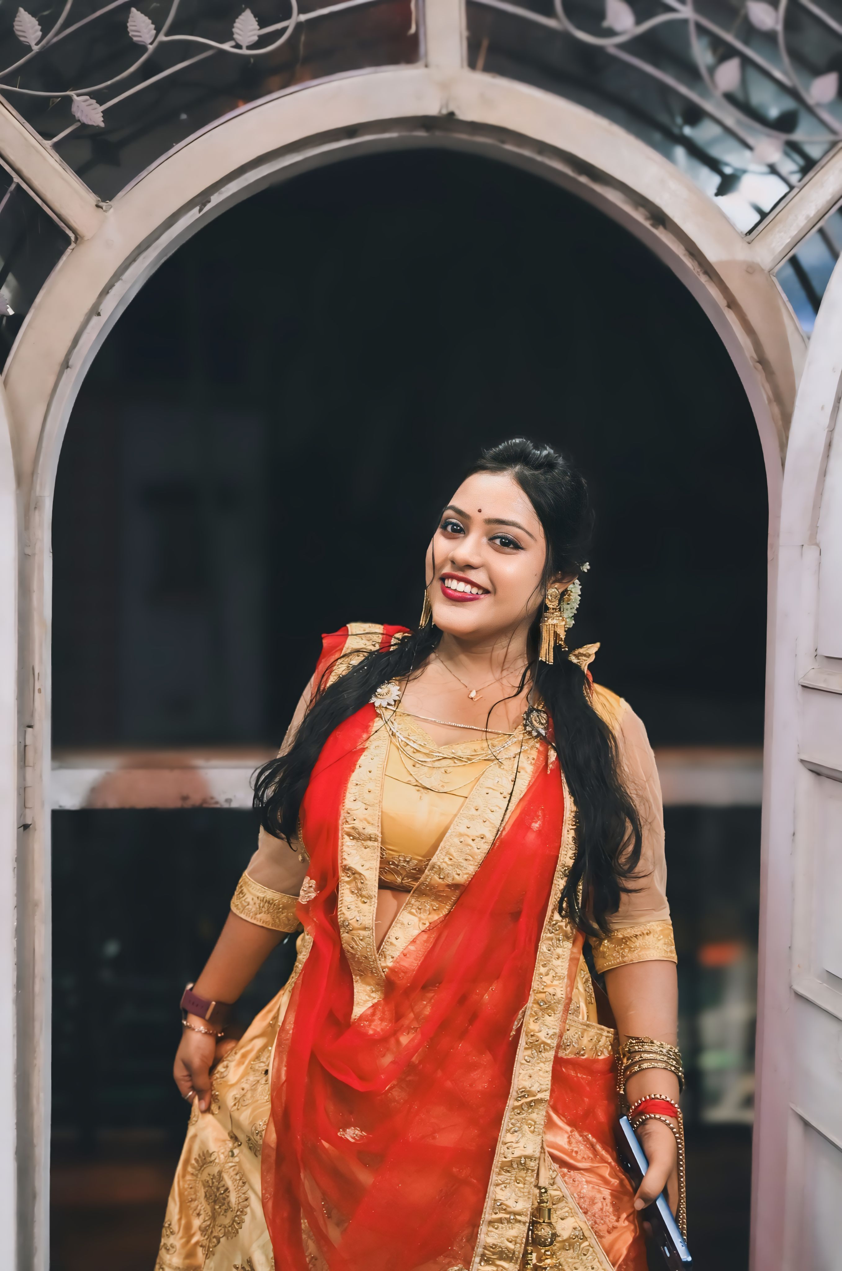 Beautiful Indian woman in traditional red and gold sari smiling warmly indoors, Kolkata, India.