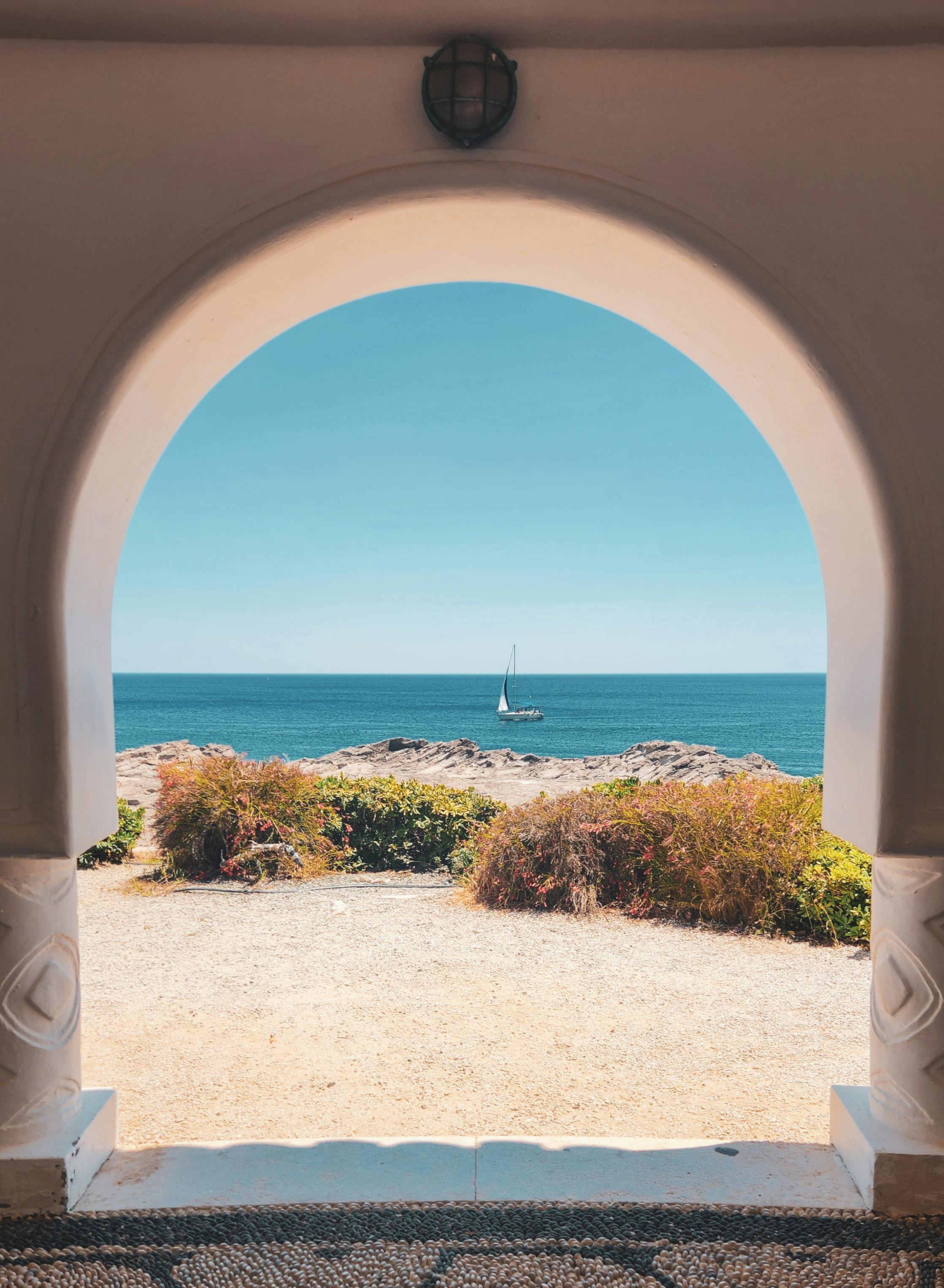 Peaceful seascape viewed through an archway with a sailboat on the horizon.