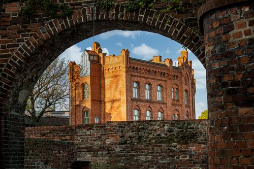 Free A gothic-style brick building seen through an ancient arch in Toruń, Poland. Stock Photo