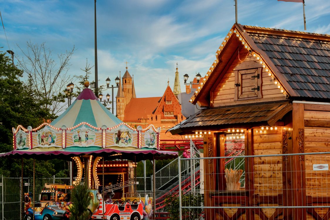 Illuminated Carousel Next to Wooden Hut in Town · Free Stock Photo