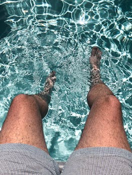 Man's legs in striped shorts enjoying the refreshing water of a swimming pool.