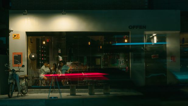 Night scene of people socializing inside a cozy cafe with blurred street lights.