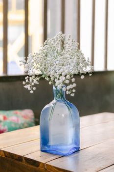 Delicate baby's breath flowers in a blue glass vase bring elegance to a simple wooden table.