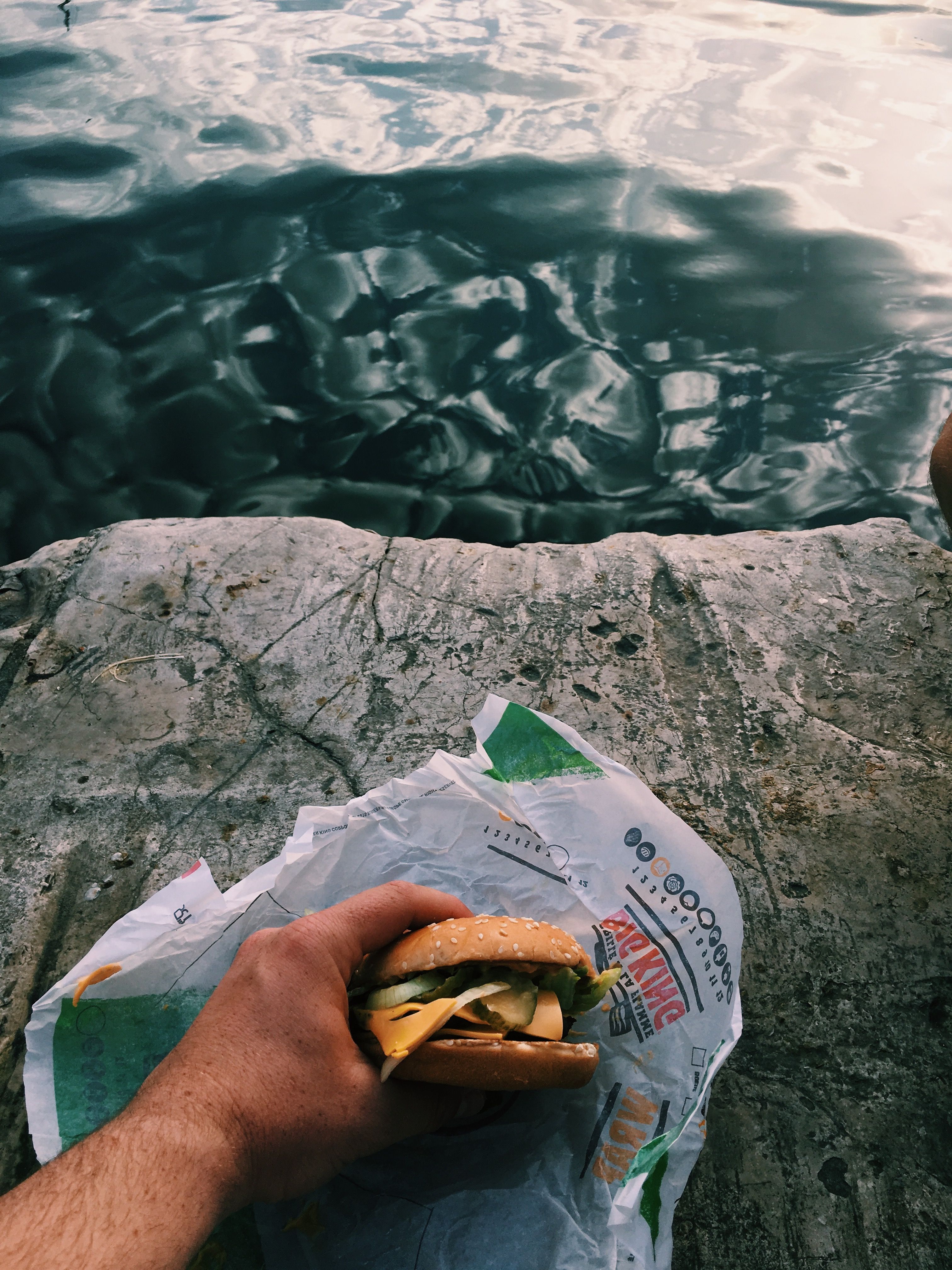Enjoying a delicious burger on a rocky shoreline with a serene ocean view.