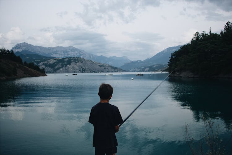 Small Boy Fishing On Lake In Mountain Area