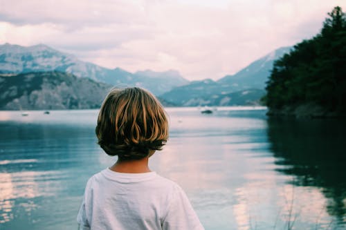 Anonymous kid admiring view on lake along mountains