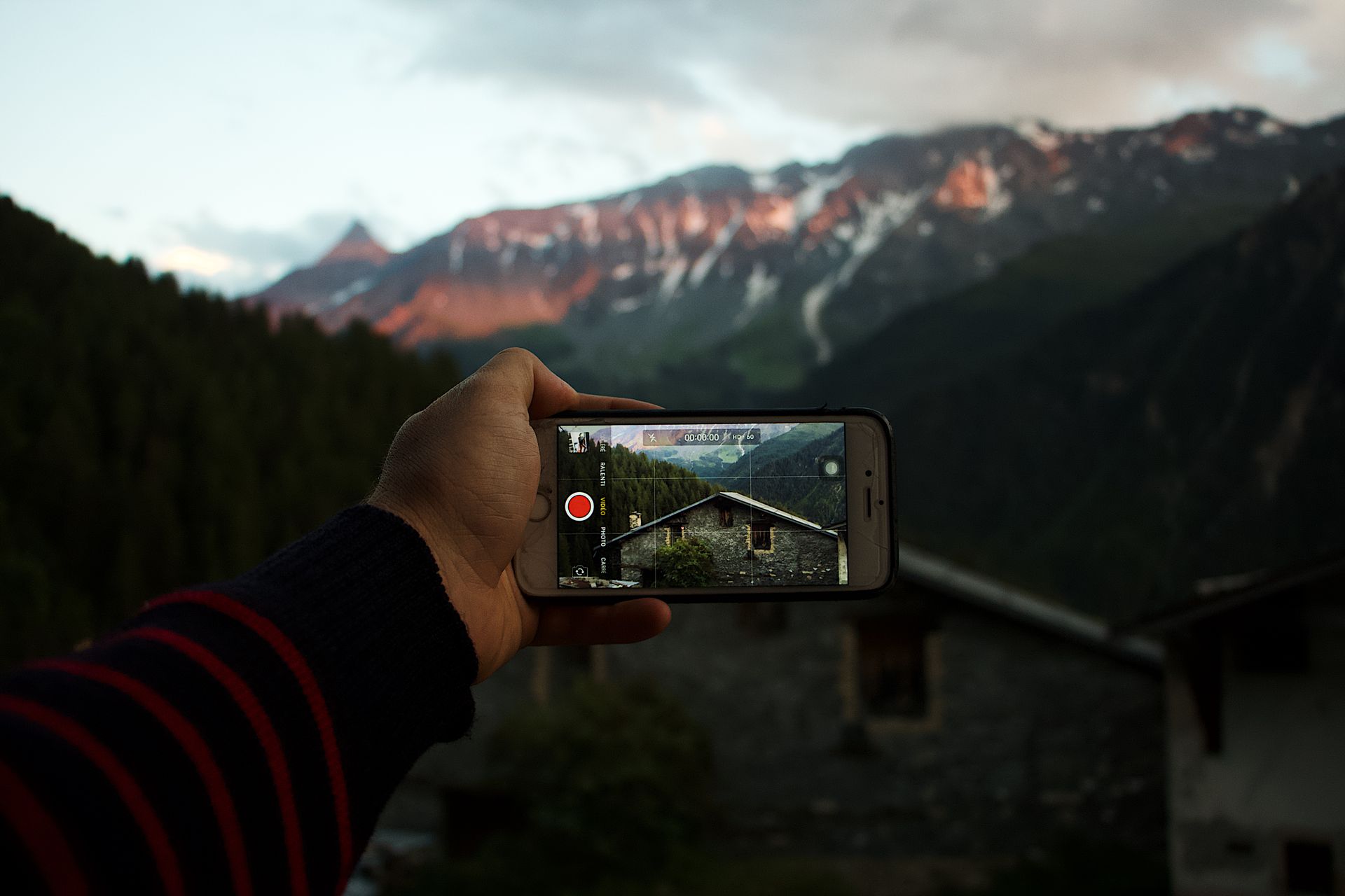 Person photographing mountain view with smartphone in serene afternoon light.