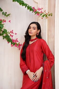 A young woman in a vibrant red traditional dress poses elegantly against a floral backdrop.