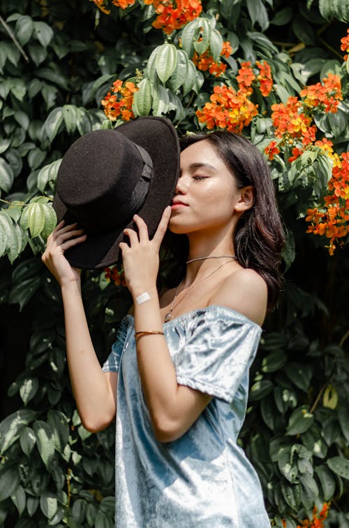 Woman Holding Black Hat Near Orange Flowers