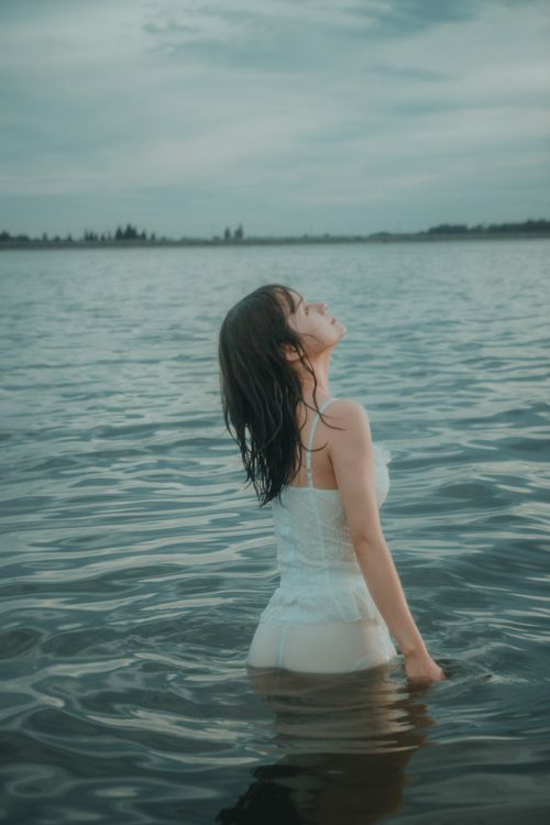 Free Elegant woman stands in calm lake waters, embracing serenity at dusk, creating a tranquil scene. Stock Photo