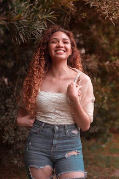 一位卷发微笑的女人，身着休闲时尚的服装，在户外摆出姿势，散发着幸福与时尚的气息