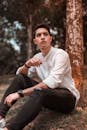 一个时尚的年轻人坐在宁静的户外，旁边有一棵树