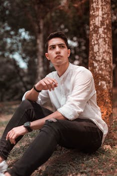 一个时尚的年轻人坐在宁静的户外，旁边有一棵树
