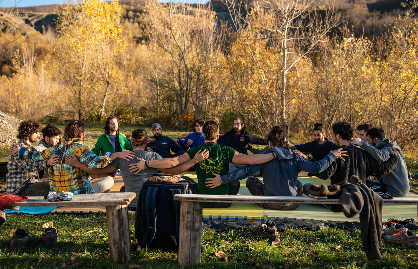 A group of people sitting in a circle on the ground outdoors in an autumn setting.