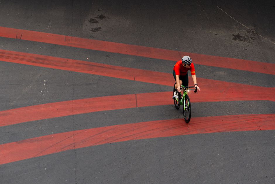 Cyclist in red jersey rides on urban asphalt road with distinct red stripes, capturing motion and speed.