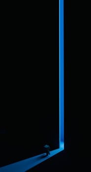 Minimalist scene with striking blue light illuminating a corridor and a figure.