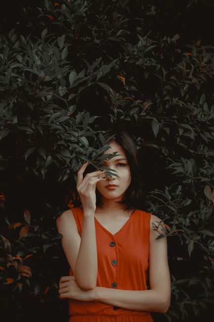 A portrait of a woman in a red dress posing with foliage in an outdoor setting.
