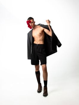 Stylish man in modern outfit poses with red flowers in studio lighting.