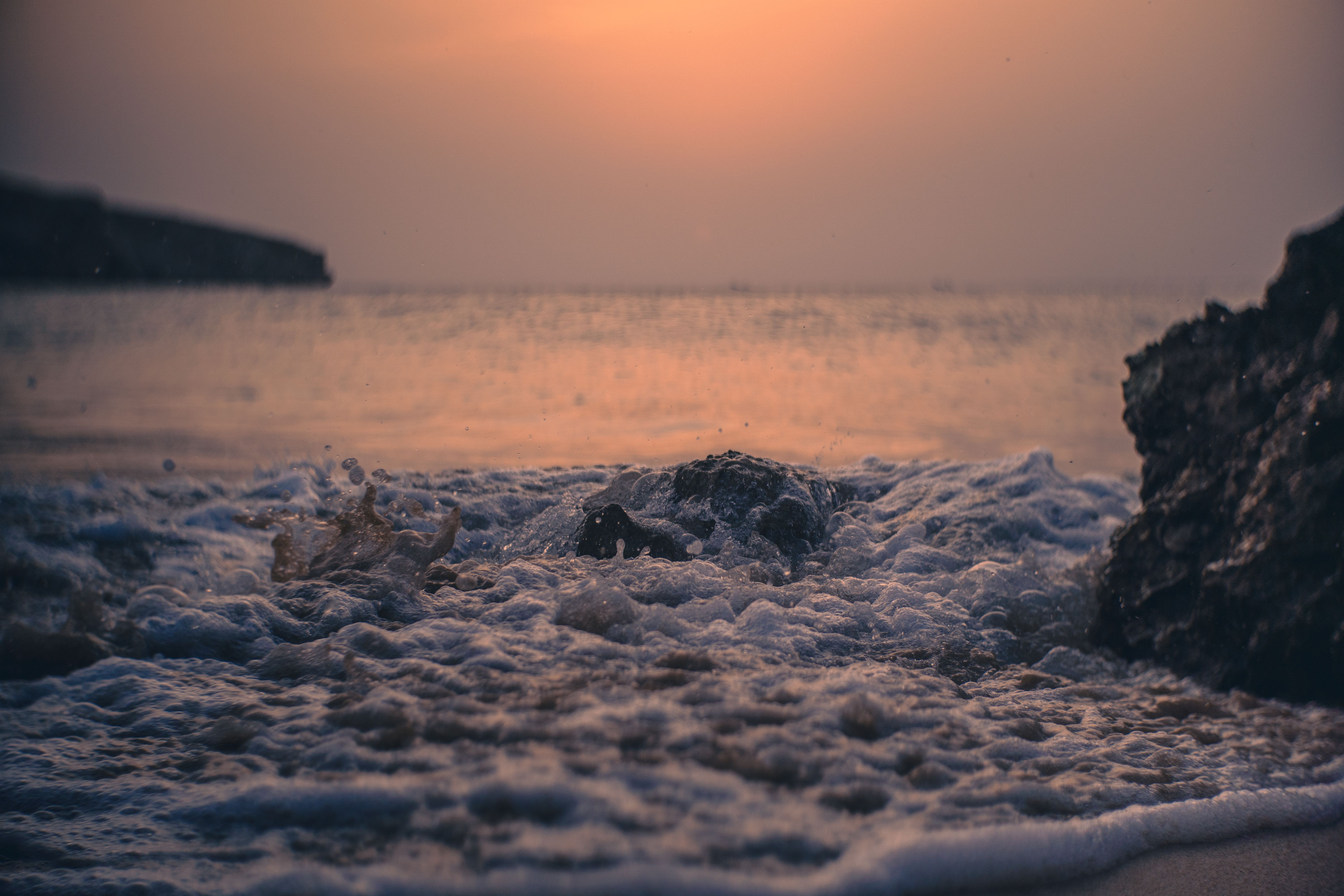 Capture the mesmerizing sunset over Muscat's rocky shoreline with waves crashing softly.