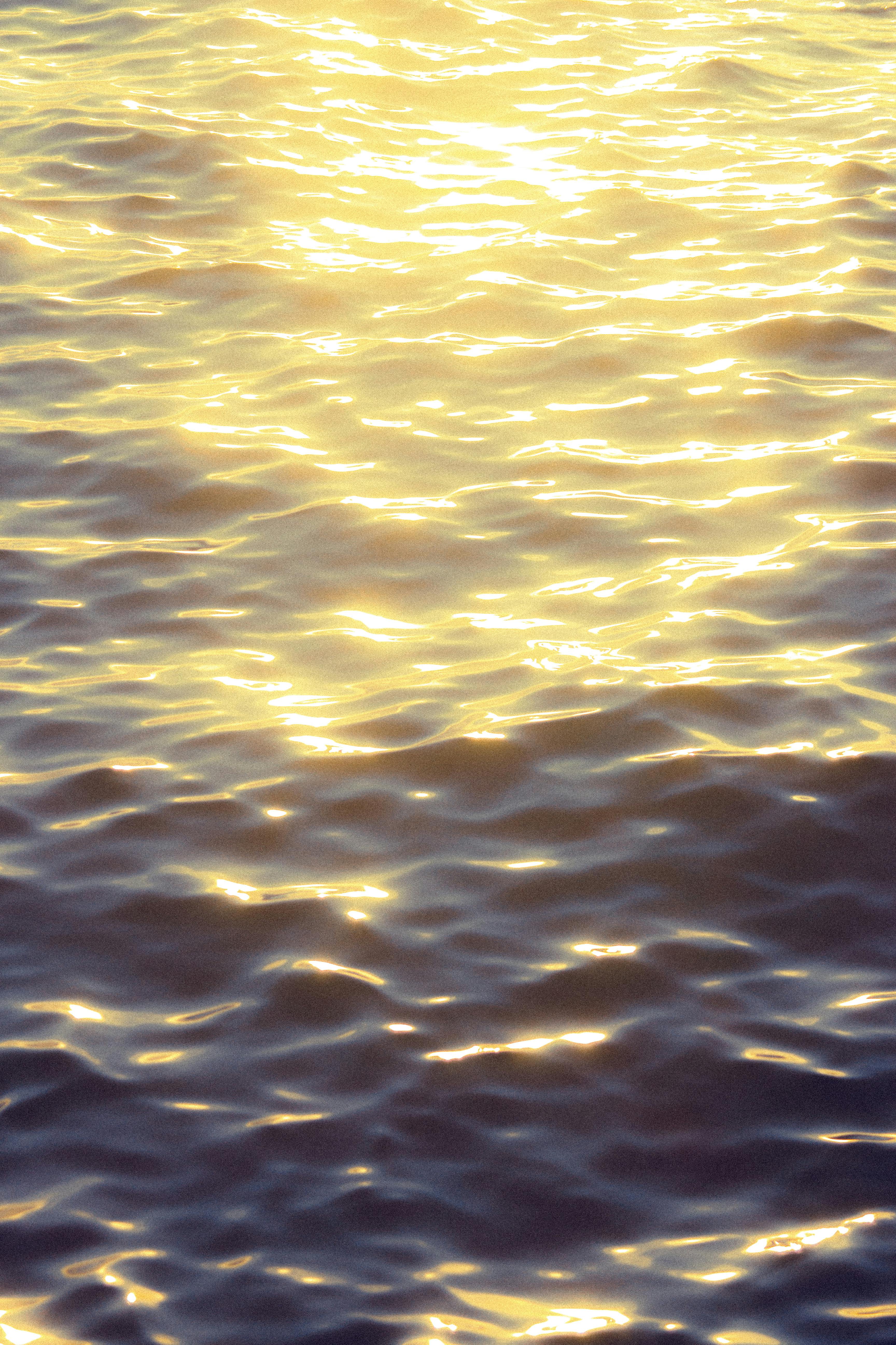 Bright sunlight reflecting on sea waves creating a shimmering effect, evoking a serene summer evening.