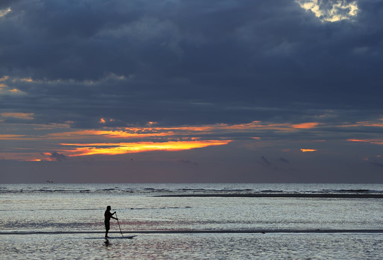 Sagoma di paddleboarder all'alba su mare calmo con riflessi