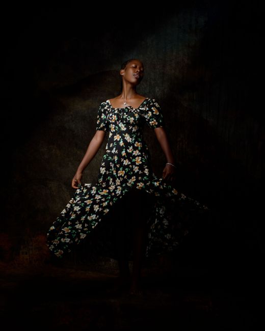 Artsy portrait of a woman in a floral gown, exuding grace and style in a dark setting.